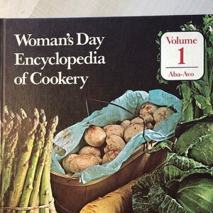 May include: A book titled "Woman's Day Encyclopedia of Cookery" with a volume number of 1. The book cover features a variety of vegetables, including asparagus, mushrooms, cabbage, onions, and tomatoes.