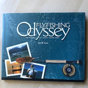 May include: A blue book cover with the title "Flyfishing Odyssey: The Pursuit of Great Game Fish" by Jon B. Cave. The cover features a map, a fishing rod, a fly fishing reel, and several photographs of people fly fishing.