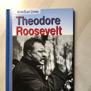 May include: A hardcover book titled "Theodore Roosevelt" from the "American Lives" series. The cover features a black and white portrait of Theodore Roosevelt and a blue, red, and white title.