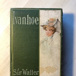 May include: A green hardcover book with the title "Ivanhoe" and the author "Sir Walter Scott" printed in white on the front cover. The cover features a vintage illustration of a woman wearing a hat.