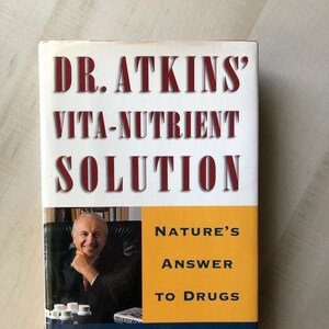May include: A book titled "DR. ATKINS' VITA-NUTRIENT SOLUTION" with the subtitle "NATURE'S ANSWER TO DRUGS" by Robert C. Atkins, M.D. The cover features a photo of Dr. Atkins.