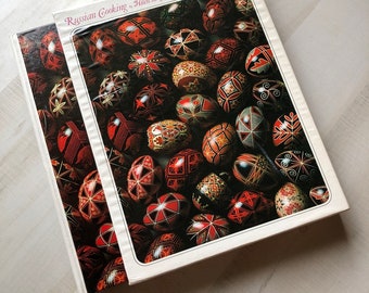 Könnte beinhalten: Zwei Hardcover-Bücher mit dem Titel "Russian Cooking" von Helen und George Papashvily. Die Einbände zeigen eine Sammlung aufwendig dekorierter Ostereier in Rot, Schwarz und Gold, die traditionelle Volkskunst präsentieren.