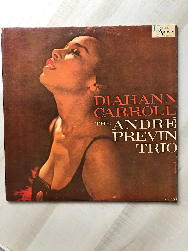 May include: A vintage vinyl record cover featuring a portrait of a woman with a microphone in front of a brown background. The text on the cover reads "Diahnne Carroll The Andre Previn Trio" and "United Artists High Fidelity".