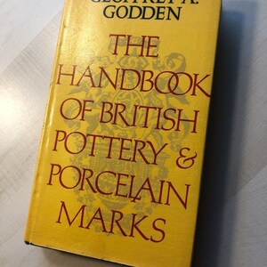 May include: A yellow book titled "The Handbook of British Pottery & Porcelain Marks" by Geoffrey A. Godden.