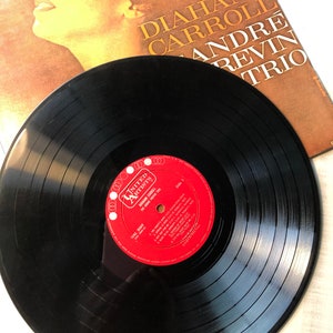 May include: A black vinyl record with a red label. The label has the text "UNITED ARTISTS" and "DIAHANN CARROLL" in white. The record is on a white surface.