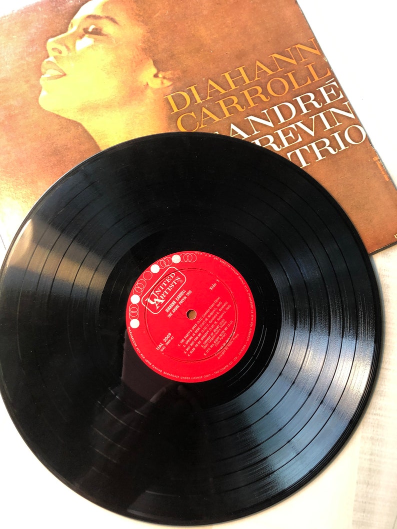 May include: A black vinyl record with a red label. The label has the text "UNITED ARTISTS" and "DIAHANN CARROLL" in white. The record is on a white surface.