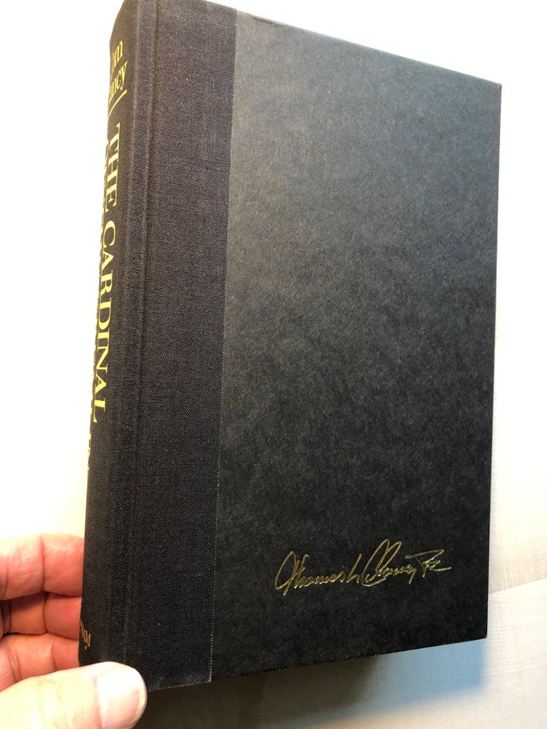 K&ouml;nnte beinhalten: Ein schwarzes Hardcover-Buch mit goldenen Lettern auf dem R&uuml;cken, die "The Cardinal" und "The Kennedy Legacy" lauten. Das Buch ist in goldener Tinte vom Autor "William Colby Jr." signiert.