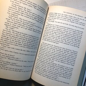 K&ouml;nnte beinhalten: Eine Nahaufnahme eines ge&ouml;ffneten Buches vor wei&szlig;em Hintergrund. Das Buch tr&auml;gt den Titel "Der Kardinal des Kremls" von Tom Clancy. Der Text auf der Seite handelt von einem U-Boot und der Cleverness der Amerikaner bei seiner Konstruktion.