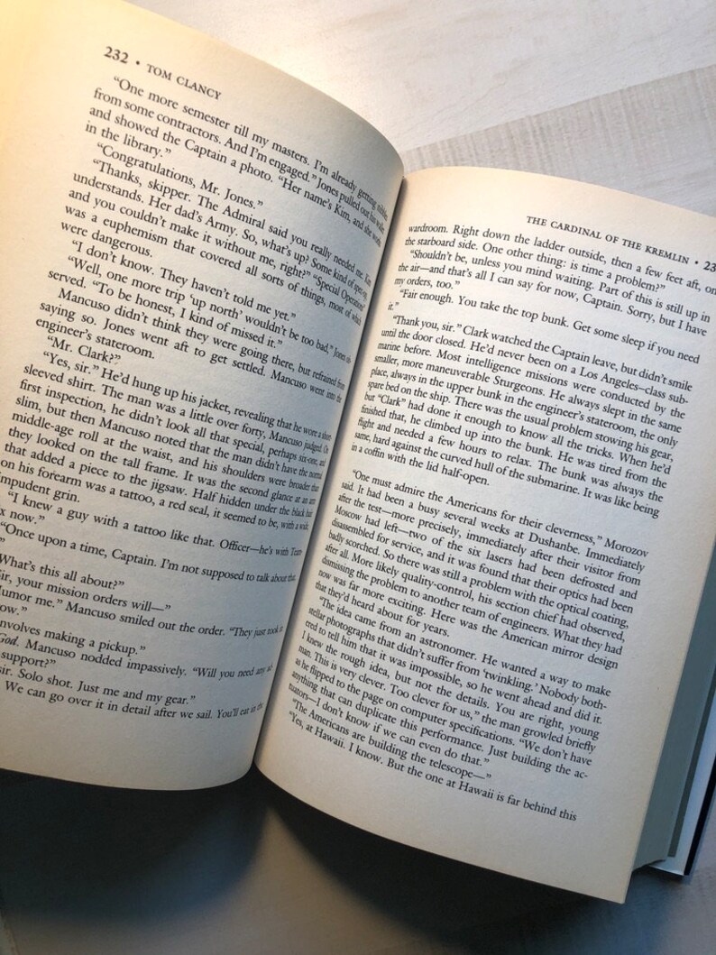 K&ouml;nnte beinhalten: Eine Nahaufnahme eines ge&ouml;ffneten Buches vor wei&szlig;em Hintergrund. Das Buch tr&auml;gt den Titel "Der Kardinal des Kremls" von Tom Clancy. Der Text auf der Seite handelt von einem U-Boot und der Cleverness der Amerikaner bei seiner Konstruktion.
