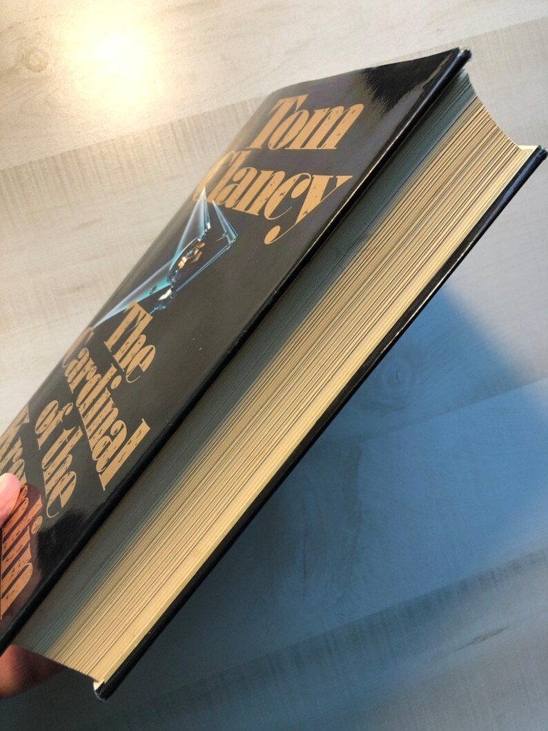 K&ouml;nnte beinhalten: Ein schwarzes Hardcover-Buch mit goldenen Lettern auf dem R&uuml;cken. Der Titel lautet "Der Kardinal des Kremls" von Tom Clancy.