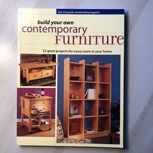 May include: Book cover with the title "build your own contemporary Furniture" and the subtitle "22 great projects for every room in your home". The cover features three images of wooden furniture: a coffee table, a bookshelf, and a rolling cart.