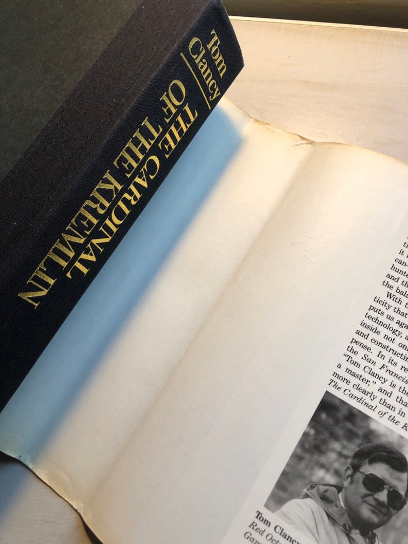 K&ouml;nnte beinhalten: Ein schwarzes Hardcover-Buch mit goldenen Lettern auf dem R&uuml;cken. Der Titel lautet "Der Kardinal des Kremls" von Tom Clancy.