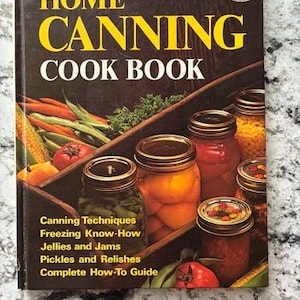 May include: A Better Homes and Gardens Home Canning Cook Book with a dark brown cover featuring a collection of glass jars filled with preserved vegetables and fruits, including green beans, tomatoes, and corn, with a price tag of $1.95.
