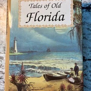 May include: A hardcover book titled Tales of Old Florida with a tan spine. The cover features a coastal illustration of a lighthouse, a small boat on the sand, and two figures. The title is printed in black text within a decorative border.