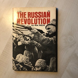 May include: A vintage paperback book cover with a black and white photo of people holding rifles. The title is "The Russian Revolution" by Ira Peck. The book cover is white with red and black text.