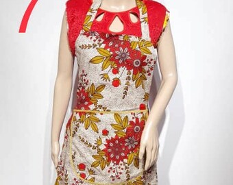 May include: A white and red floral apron with a red sleeveless top underneath. The apron has a large pocket on the front and a yellow trim. The model is wearing the apron and top.