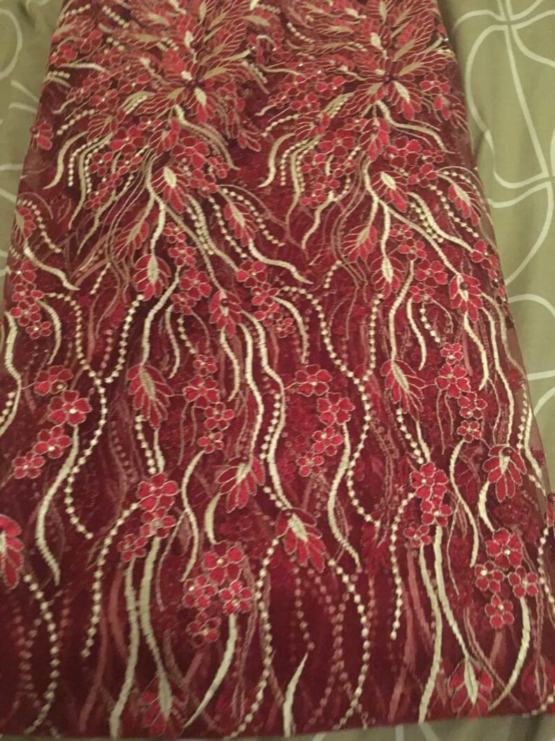 May include: Red lace fabric with gold embroidery featuring a floral pattern.