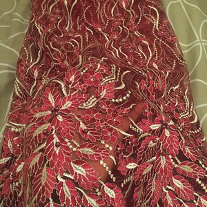 May include: Red and gold lace fabric with a floral pattern. The lace is delicate and intricate, with small beads scattered throughout.
