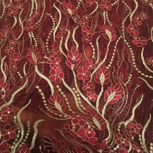 May include: Red lace fabric with a floral pattern and gold accents. The fabric is sheer and has a delicate texture.