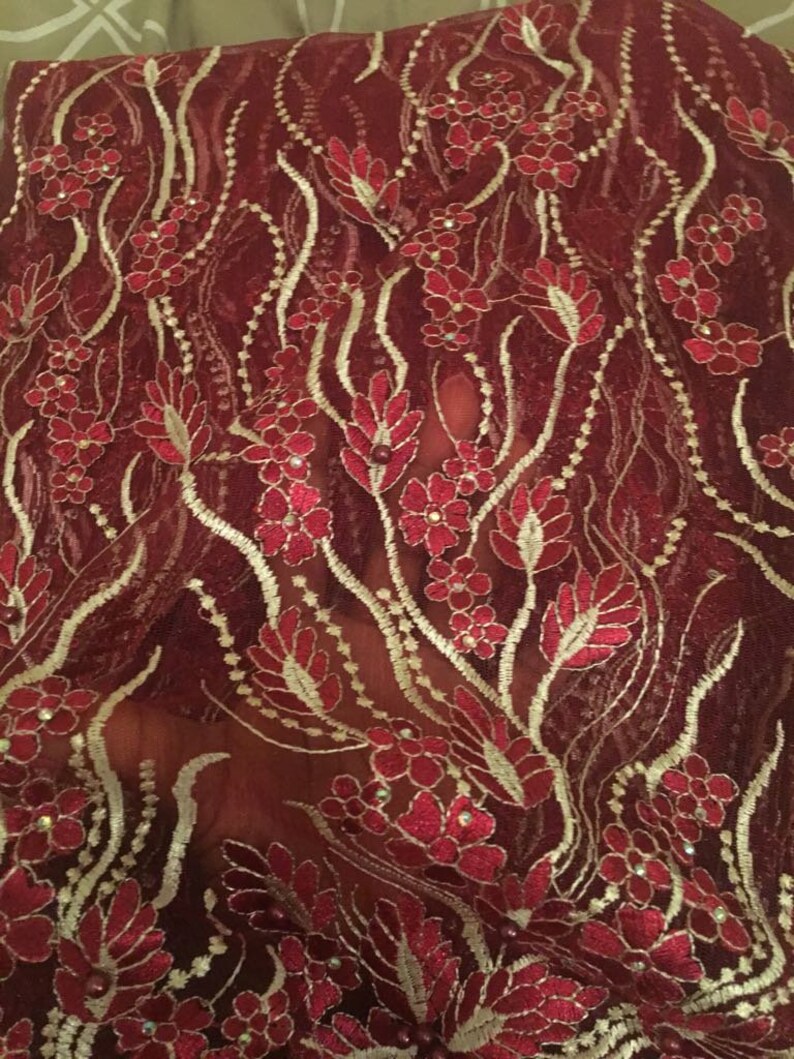 May include: Red lace fabric with a floral pattern and gold accents. The fabric is sheer and has a delicate texture.