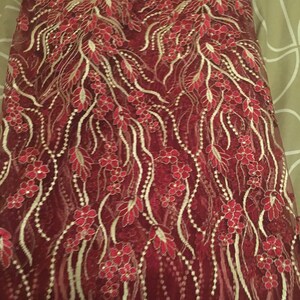 May include: Red and gold lace fabric with a floral pattern. The fabric has a delicate, intricate design with small flowers and leaves.