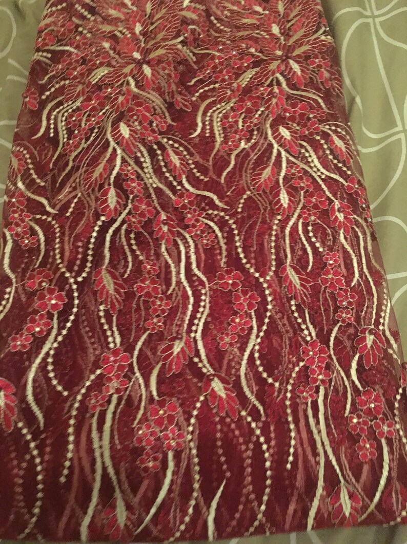May include: Red and gold lace fabric with a floral pattern. The fabric has a delicate, intricate design with small flowers and leaves.