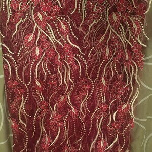 May include: Burgundy lace fabric with gold embroidery featuring a floral pattern.