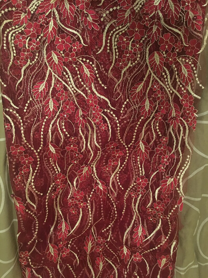 May include: Burgundy lace fabric with gold embroidery featuring a floral pattern.