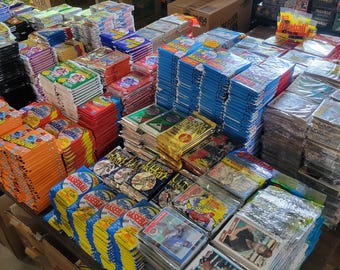 May include: A large assortment of vintage trading card packs and boxes, including baseball cards, displayed on a table. The packs are in various colors, including blue, orange, red, and yellow. Some are sealed in plastic.