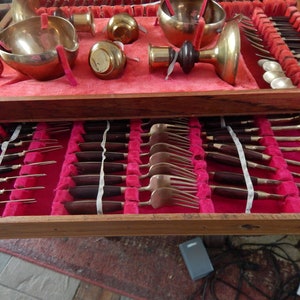 Puede incluir: Un juego de cubiertos de madera con interior de terciopelo rojo. El juego incluye varias piezas de servir, tenedores, cucharas y cuchillos con mangos de madera oscura y metal dorado. La sección superior contiene cuencos para servir y otras piezas de servir de color latón.
