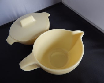 May include: A set of two yellow ceramic creamer and sugar bowls. The sugar bowl has a lid with a handle.