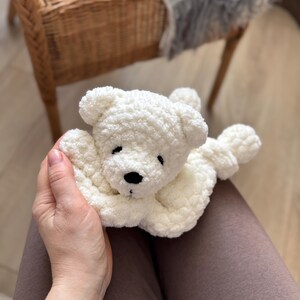 Pode incluir: Um urso de pel&uacute;cia branco de croch&ecirc; feito &agrave; m&atilde;o com nariz e olhos pretos. O urso est&aacute; deitado com os bra&ccedil;os estendidos. O brinquedo macio e fofo &eacute; um item reconfortante para crian&ccedil;as.