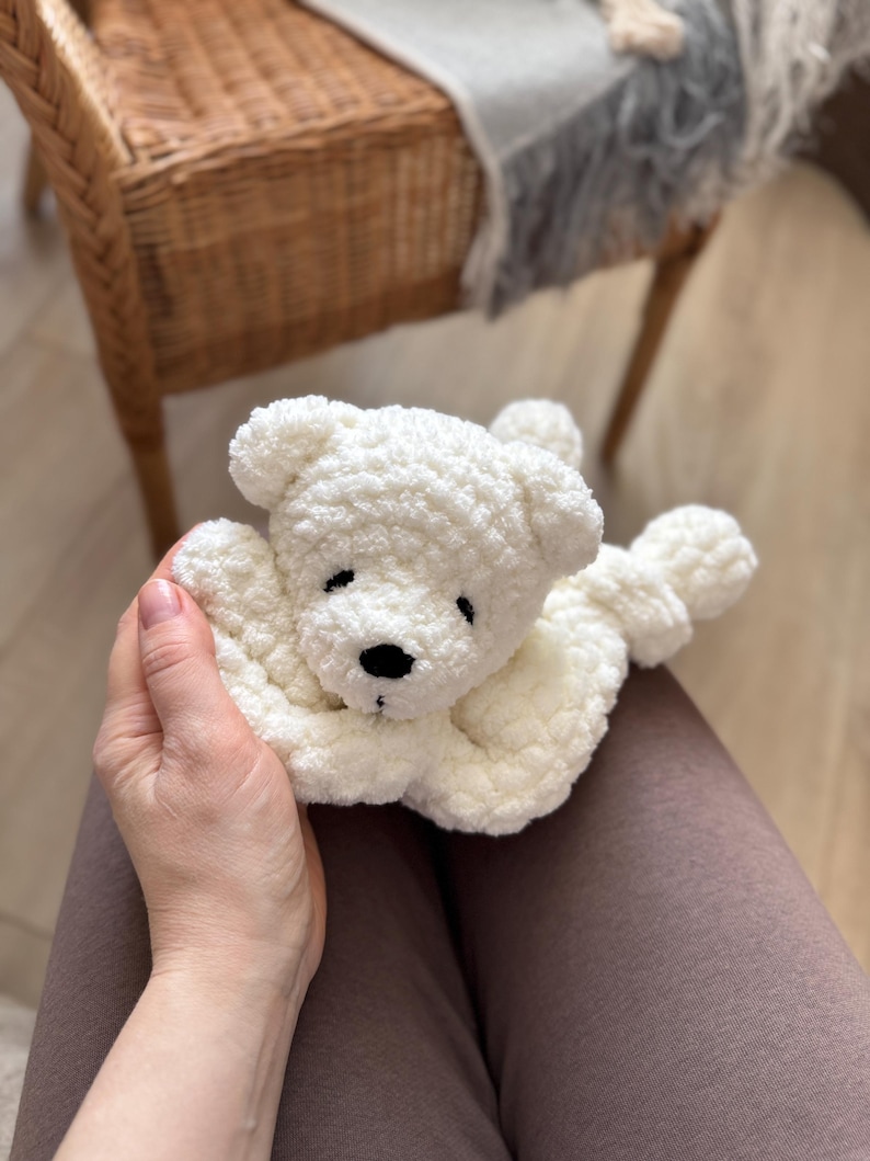 Pode incluir: Um urso de pel&uacute;cia branco de croch&ecirc; feito &agrave; m&atilde;o com nariz e olhos pretos. O urso est&aacute; deitado com os bra&ccedil;os estendidos. O brinquedo macio e fofo &eacute; um item reconfortante para crian&ccedil;as.