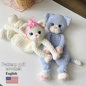 Puede incluir: Dos muñecos de gato hechos a mano con ganchillo. Uno es blanco con un lazo y una diadema rosas, el otro es azul claro. Ambos tienen narices y patas rosas, y ojos azules. La imagen incluye el texto "Pattern pdf crochet English".
