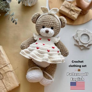 Könnte beinhalten: Ein gehäkelter Teddybär, der ein weißes Kleid mit roten Herzen, ein passendes Stirnband und weiße Ballerinas trägt. Der Bär ist hellbraun mit einer weißen Schnauze. Der Text auf dem Bild lautet "Crochet clothing set" und "Pattern pdf English".