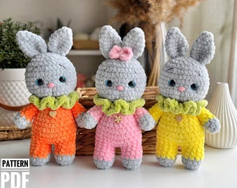 Puede incluir: Tres juguetes de conejo de crochet gris que llevan atuendos de diferentes colores. El conejo de la izquierda lleva naranja, el del medio lleva rosa y el de la derecha lleva amarillo.