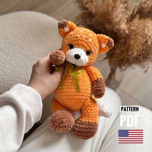 Puede incluir: Juguete de peluche de zorro naranja tejido a crochet con detalles blancos y una cinta verde. El juguete está siendo sostenido por una mano. El texto "PATTERN PDF" es visible en la imagen.
