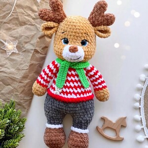 May include: A handmade crochet reindeer doll with brown antlers, a red and white striped sweater, and gray pants. The reindeer has blue eyes, a green scarf, and brown shoes. A wooden rocking horse is next to the doll.