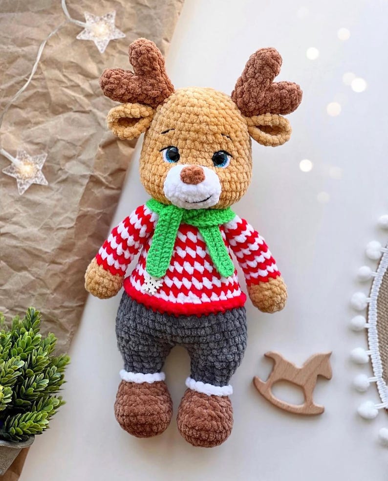 May include: A handmade crochet reindeer doll with brown antlers, a red and white striped sweater, and gray pants. The reindeer has blue eyes, a green scarf, and brown shoes. A wooden rocking horse is next to the doll.