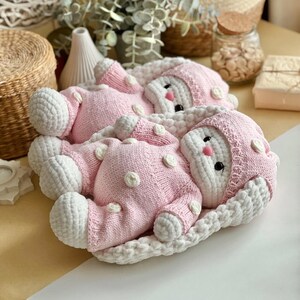 Puede incluir: Dos mu&ntilde;ecas de beb&eacute; hechas a mano con ganchillo en rosa y blanco. Las mu&ntilde;ecas visten trajes rosas con lunares blancos y gorros a juego. Est&aacute;n tumbadas sobre una manta blanca de ganchillo. Las mu&ntilde;ecas tienen ojos negros y mejillas rosas.