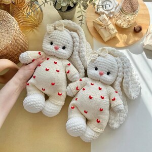 Puede incluir: Dos mu&ntilde;ecos de conejito de ganchillo hechos a mano, de color crema, con largas orejas ca&iacute;das y peque&ntilde;os acentos de coraz&oacute;n rojo. Cada conejito tiene un peque&ntilde;o lazo en la cabeza y una nariz rosa. Los conejitos son suaves y tiernos.
