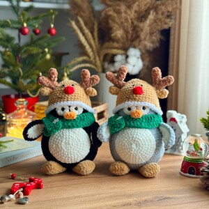 May include: Two handmade crochet penguin figures, one black and white, the other gray and white. Both wear reindeer hats with brown antlers and red noses, and green scarves. They are Christmas-themed decorations.