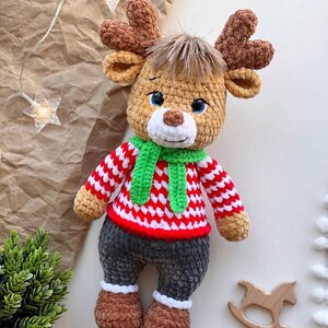 May include: A handmade crochet reindeer doll with brown antlers, a green scarf, and a red and white striped sweater. The reindeer has gray pants, brown shoes, and blue eyes. A charming holiday decoration.