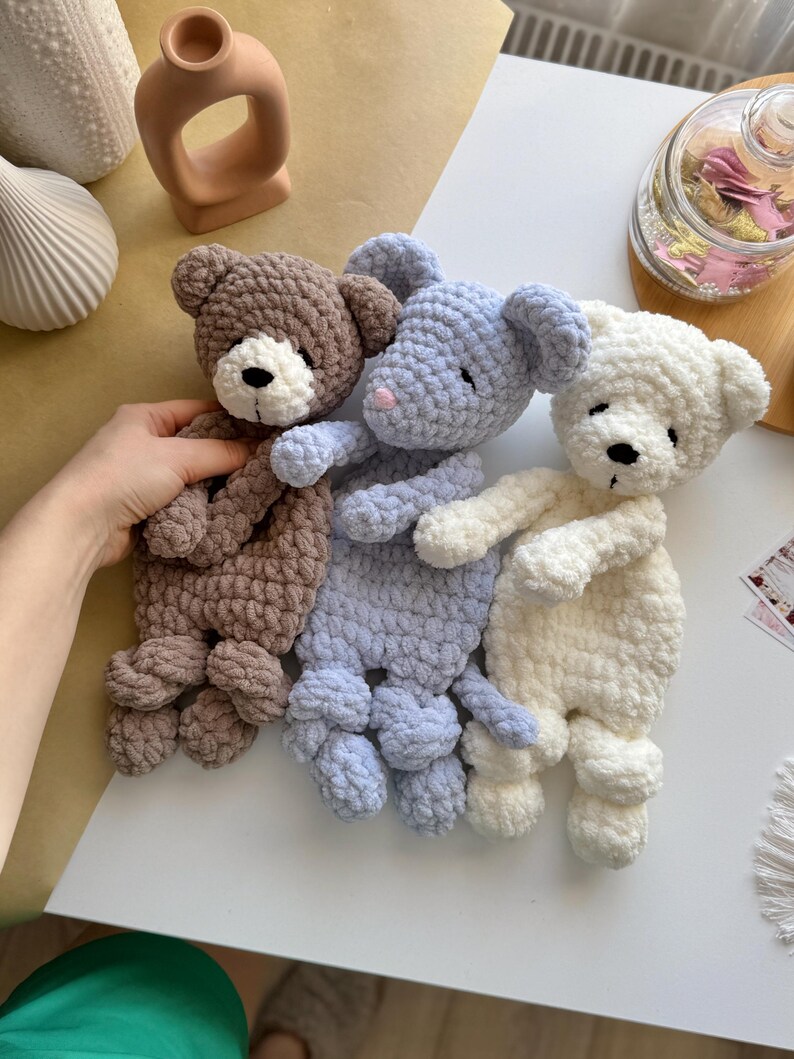 Pode incluir: Tr&ecirc;s ursos de pel&uacute;cia de croch&ecirc; feitos &agrave; m&atilde;o em marrom, azul e branco. Cada urso tem um nariz preto e um focinho branco. Os ursos est&atilde;o em uma superf&iacute;cie branca. Os ursos s&atilde;o macios e fofinhos.