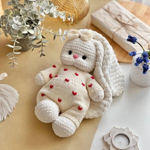 Puede incluir: Una mu&ntilde;eca de conejo de ganchillo blanco hecha a mano, con orejas largas y ca&iacute;das y un peque&ntilde;o lazo. El conejo lleva un atuendo color crema adornado con corazones rojos. La mu&ntilde;eca tiene una nariz rosa y ojos negros. Un juguete suave y encantador para ni&ntilde;os.