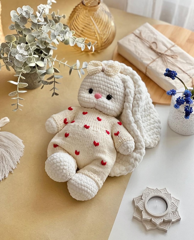 Puede incluir: Una mu&ntilde;eca de conejo de ganchillo blanco hecha a mano, con orejas largas y ca&iacute;das y un peque&ntilde;o lazo. El conejo lleva un atuendo color crema adornado con corazones rojos. La mu&ntilde;eca tiene una nariz rosa y ojos negros. Un juguete suave y encantador para ni&ntilde;os.