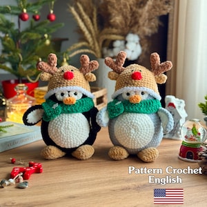 May include: Two handmade crochet penguin figures, one black and white, the other gray and white, each wearing a reindeer hat and green scarf. The penguins are on a wooden surface. The image includes text that says "Pattern Crochet English".