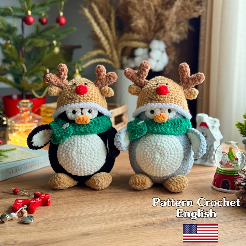 May include: Two handmade crochet penguin figures, one black and white, the other gray and white, each wearing a reindeer hat and green scarf. The penguins are on a wooden surface. The image includes text that says "Pattern Crochet English".