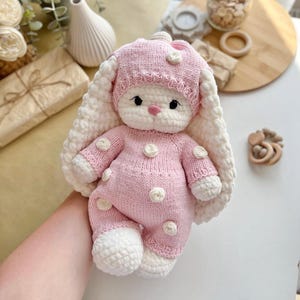 Puede incluir: Una mu&ntilde;eca de conejito de ganchillo rosa y blanco hecha a mano. El conejito viste un conjunto rosa con lunares blancos y un gorro a juego. El conejito tiene orejas largas y ca&iacute;das y una expresi&oacute;n dulce.