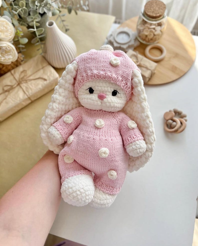 Puede incluir: Una mu&ntilde;eca de conejito de ganchillo rosa y blanco hecha a mano. El conejito viste un conjunto rosa con lunares blancos y un gorro a juego. El conejito tiene orejas largas y ca&iacute;das y una expresi&oacute;n dulce.